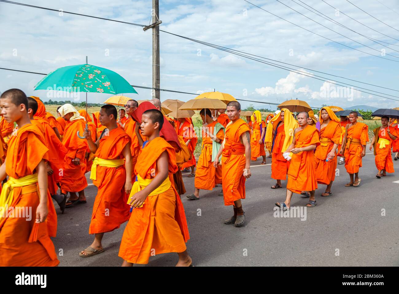 Lokale buddhistische Mönche in traditionellen Safranfarben gehen entlang einer Straße außerhalb von Chiang Rai, einer Stadt im Norden Thailands Stockfoto