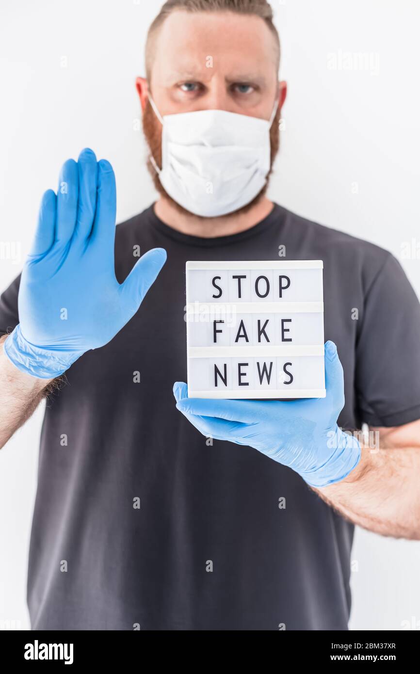 Fake News Infosemics during Covid-19 Pandemie Concept. Mann trägt Schutzmaske und medizinische Handschuhe an den Händen halten Leuchtkasten mit Text Stop Fake ne ne Stockfoto