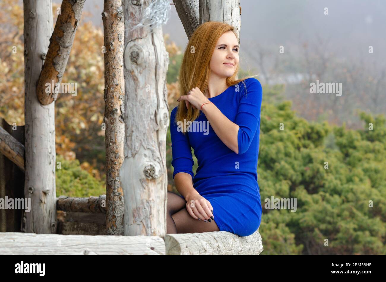 Schönes Mädchen in hellblauem Kleid sitzt auf einer Holzterrasse und blickt in die Ferne Stockfoto