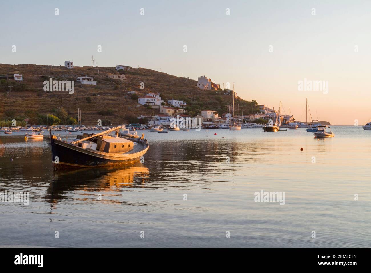 Nachmittag auf der Insel Kea in Griechenland. Ein kleiner Hafen und ein altes Fischerboot im Vordergrund. Es ist goldene Stunde und das Meer ist friedlich. Stockfoto