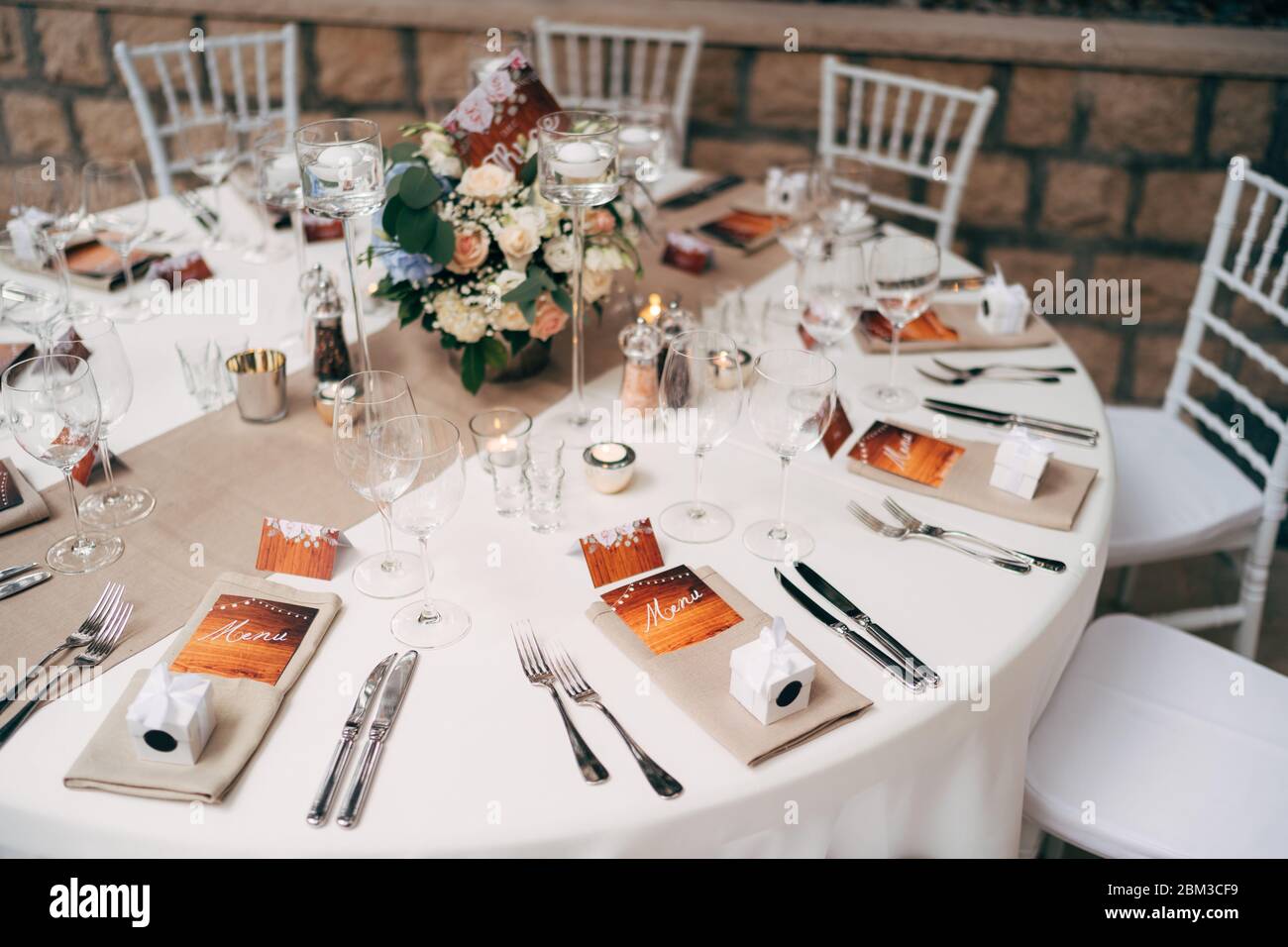 Empfang am Tisch für Hochzeitsessen. Runder Tisch mit weißer Tischdecke mit braunem Läufer auf Tisch. Wien in braunen Servietten verschachtelt, ist ein Blumenstrauß Stockfotografie