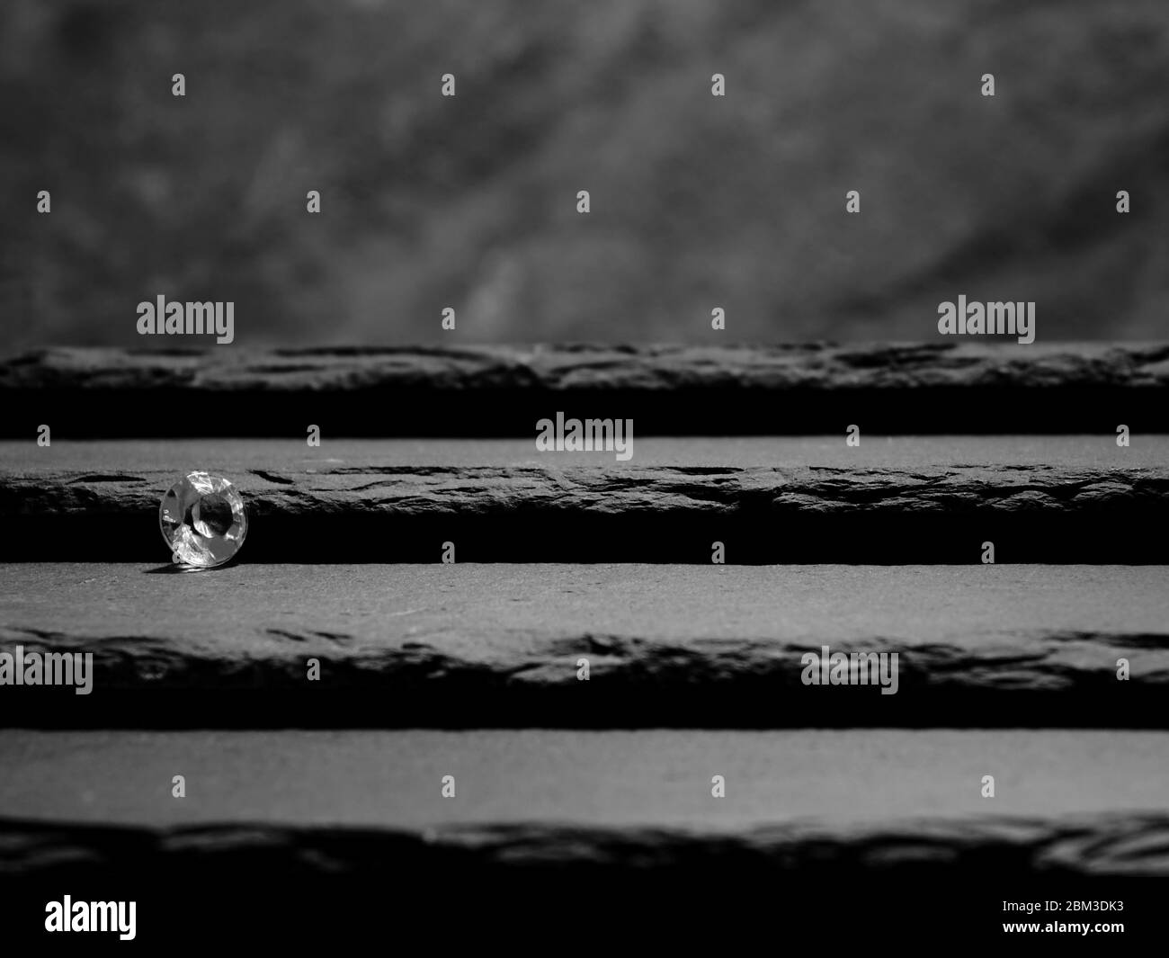Ein einzelner Diamant zeigt den Facettenschnitt des Steins, auf Schiefer-Stufen gelegt, die zu einem unscharfen Hintergrund führen Stockfoto