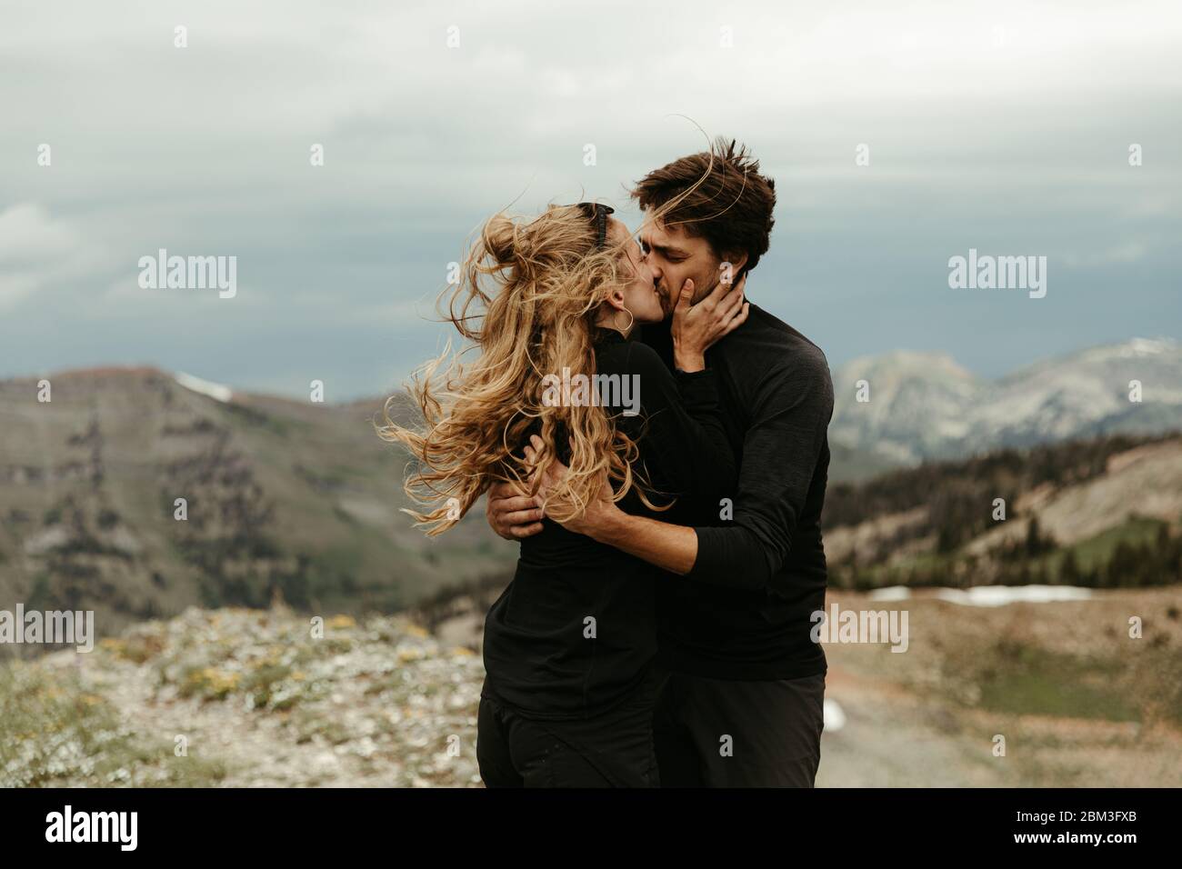 Neu verlobt weißes Paar in ganz schwarz Kuss auf gekleidet Windiger Grat Stockfoto