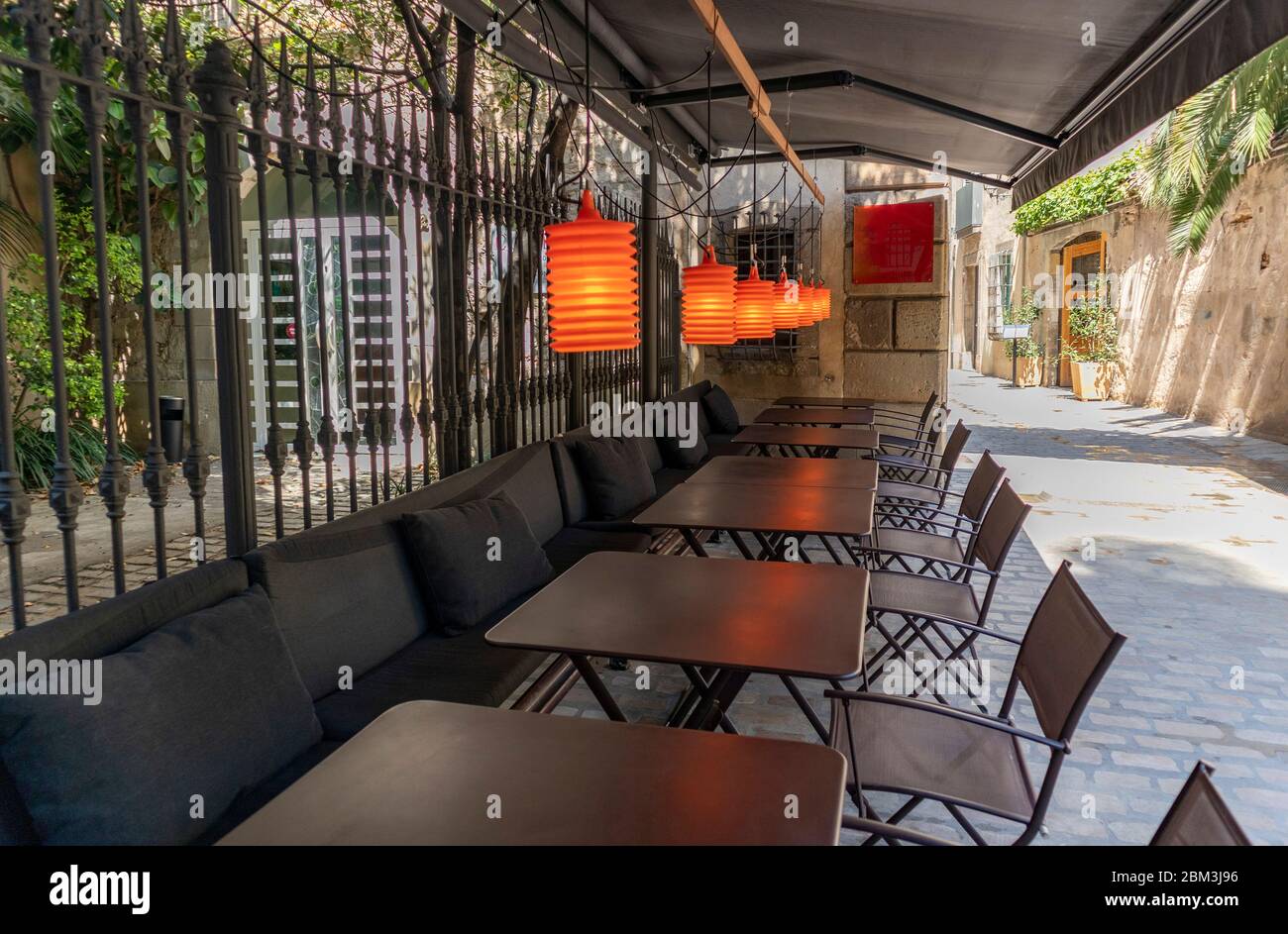 Tische, Stühle und orangefarbene Lichter auf einer Terrasse in der Straße Stockfoto