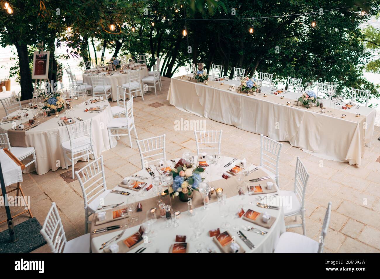 Empfang am Tisch für Hochzeitsessen. Runde Tische mit weißen Tischdecken, braunen Läufern, Blumensträußen, Chiavari-Stühlen, Menü in Serviette eingeschlossen Stockfotografie