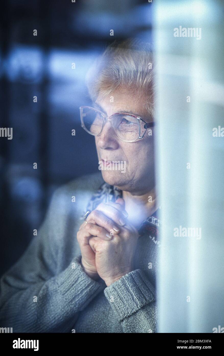 Ältere Frau hinter dem Fenster mit Besorgnis. Stockfoto