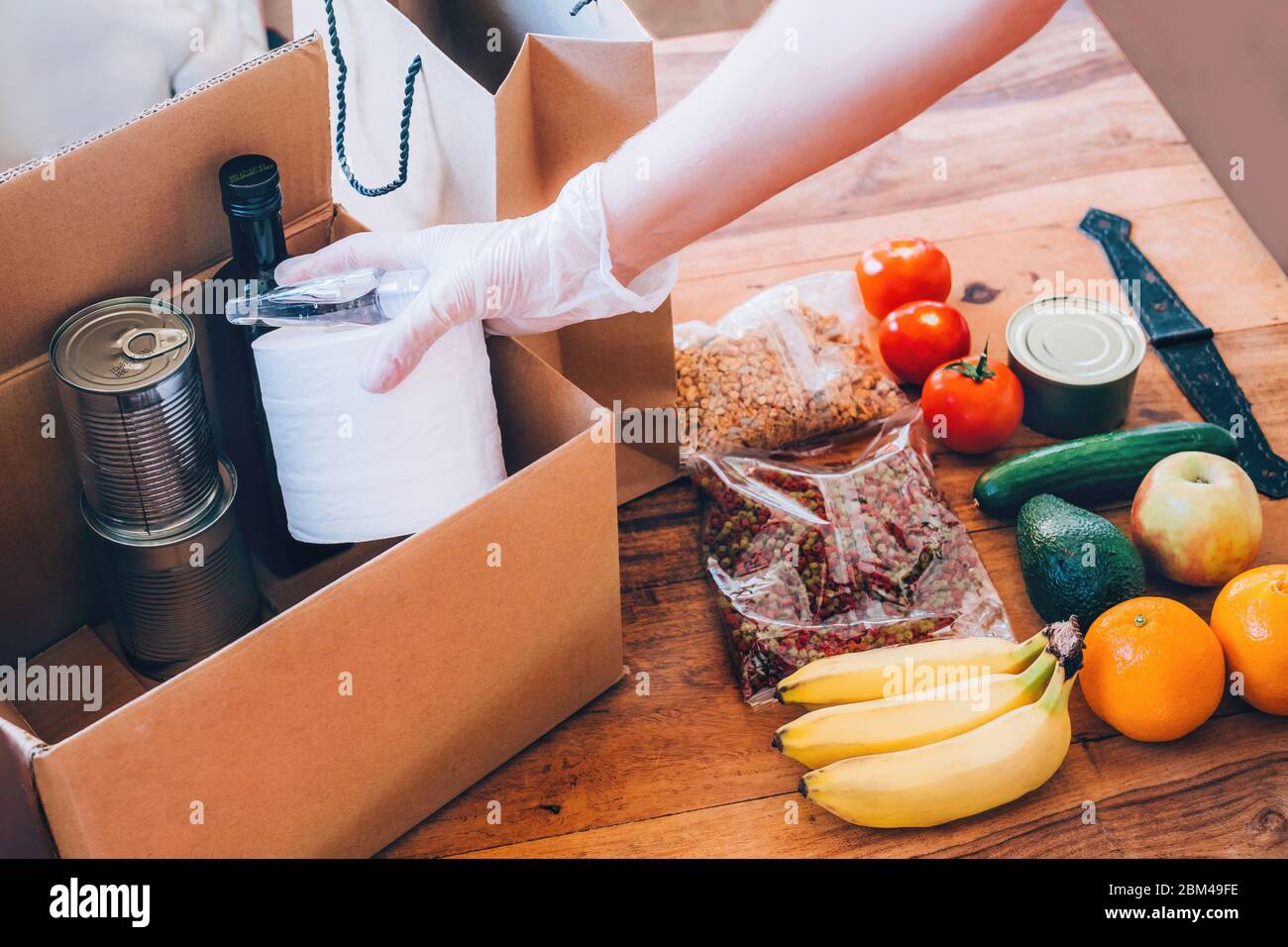Die Hand einer Frau legt Lebensmittel, Toilettenpapier und Handdesinfektionsmittel zur Spende in die corton-Box. Covid-19 Ausbruch, Selbstisolierung, Lieferkonzept. Stockfoto