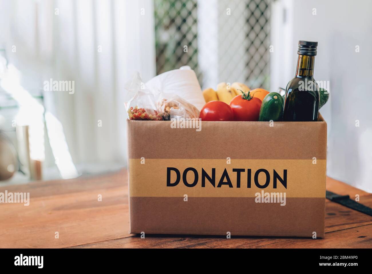 Box mit Lebensmitteln, Toilettenpapier und Handdesinfektionsmittel auf dem Holztisch. Flaches Lay. Covid-19 Ausbruch, Selbstisolierung, Lieferung, Spendenkonzept. Stockfoto