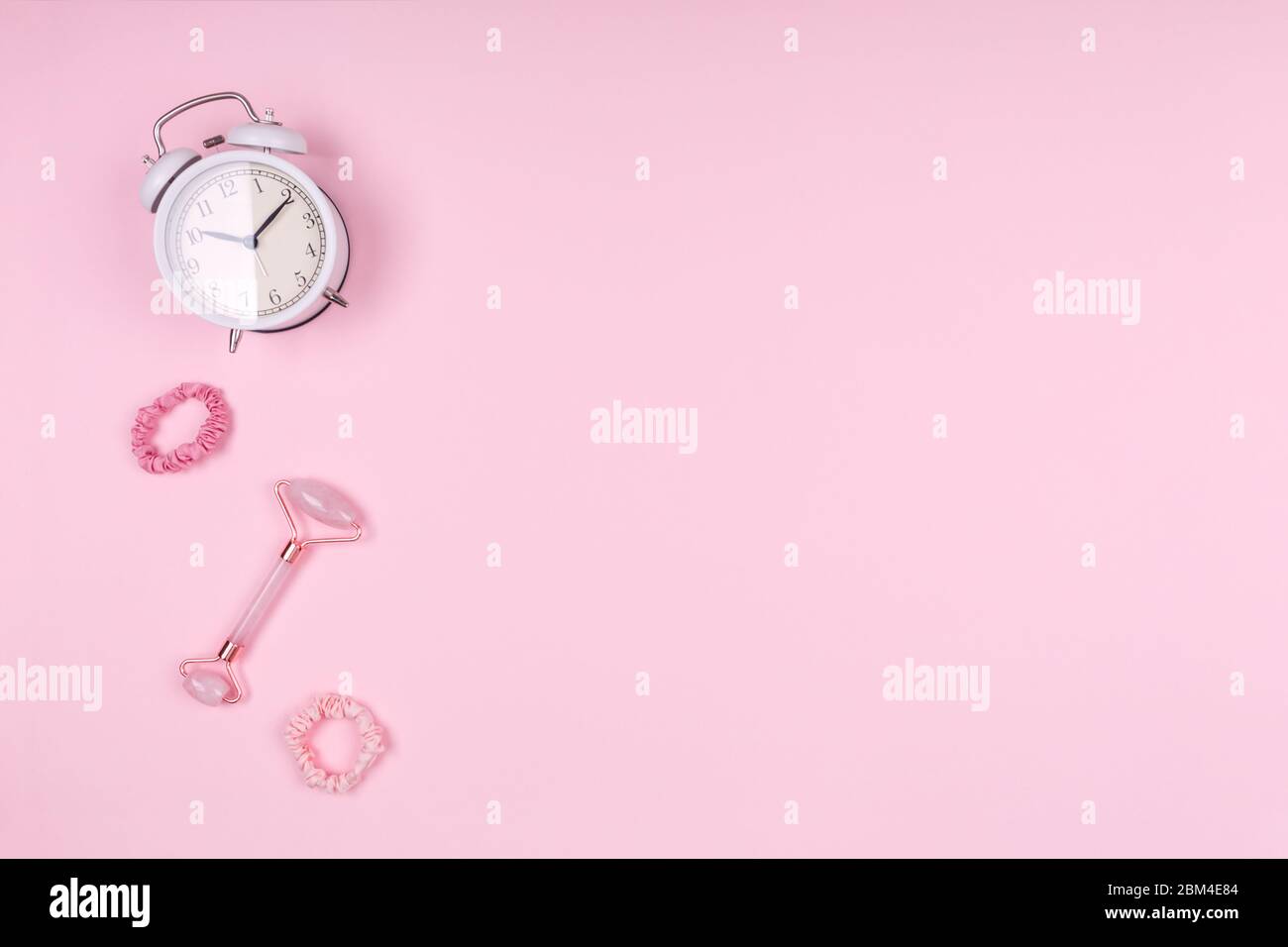 Jade Face Roller mit weißer Uhr und rosa Accessoires. Beauty Time, Selfcare und Beauty Accessoires Konzept. Platz für Text Stockfoto