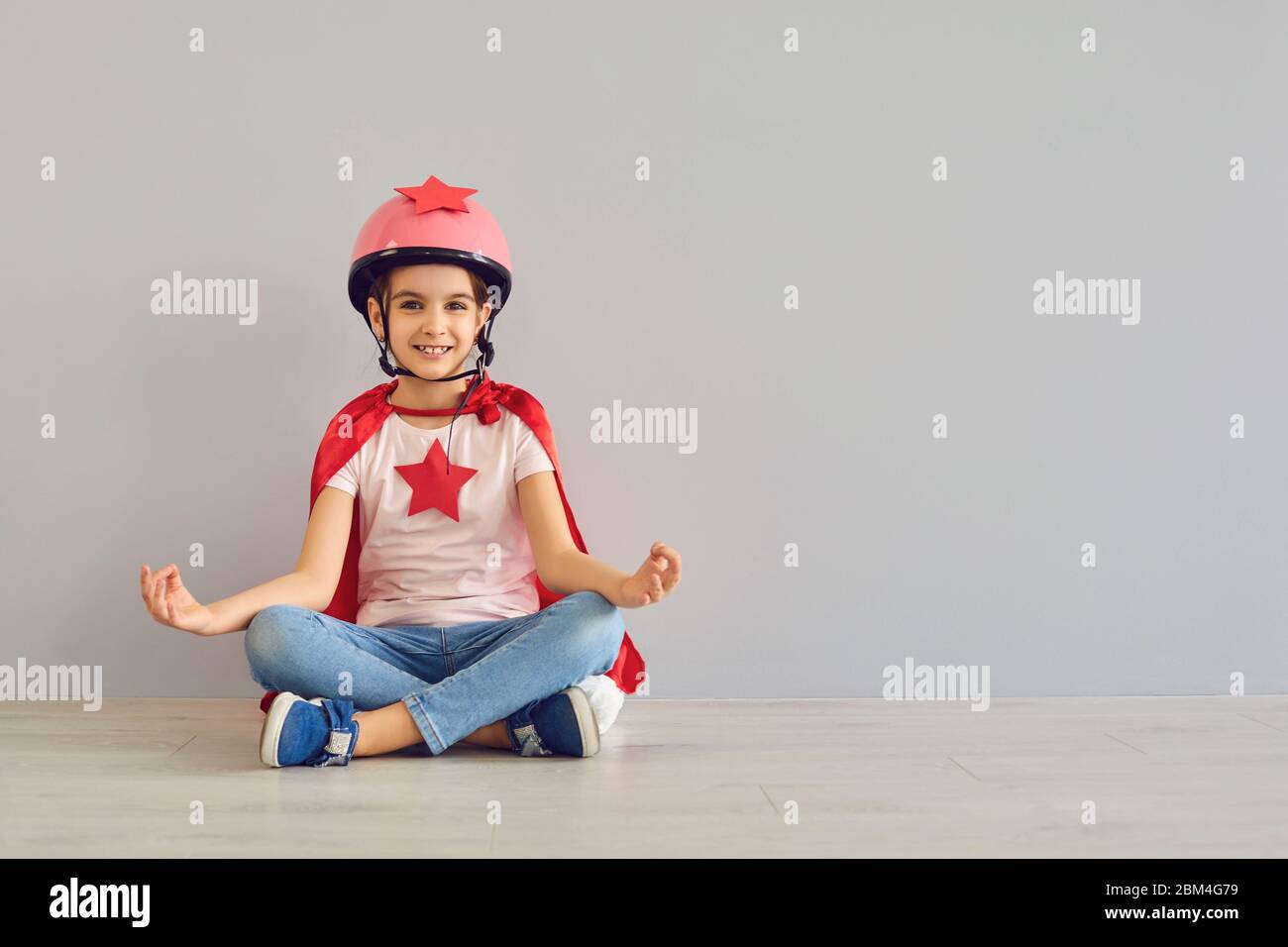 Lustige Baby-Superhelden lachen, während sie auf dem Boden in Lotusposition sitzen. Konzept lustige Held lächelnd Traum Führer träumen. Lustige Kinder Yoga. Stockfoto