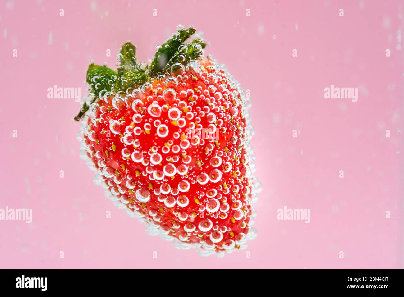 Rote Erdbeerfrucht, die im Wasser auf rosa Hintergrund schwebt. Hochwertige kommerzielle Food-Fotografie. Konzept für frische Getränke. Stockfoto
