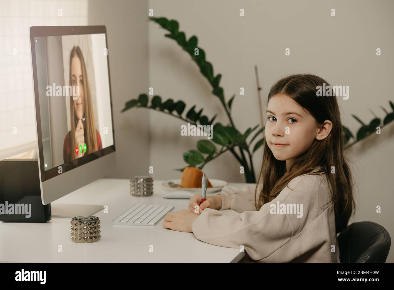 Fernunterricht. Ein junges Mädchen mit langen Haaren, das fernab von ihrer Lehrerin online studiert. Ein hübsches Kind lernt eine Lektion mit einem Desktop-Comput Stockfoto