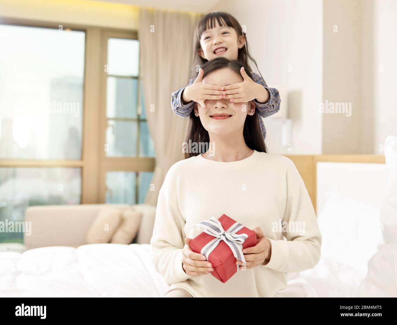 Happy Little Asian Girl Mutter ein Geschenk und bedeckt Mutter die Augen mit Händen Stockfoto