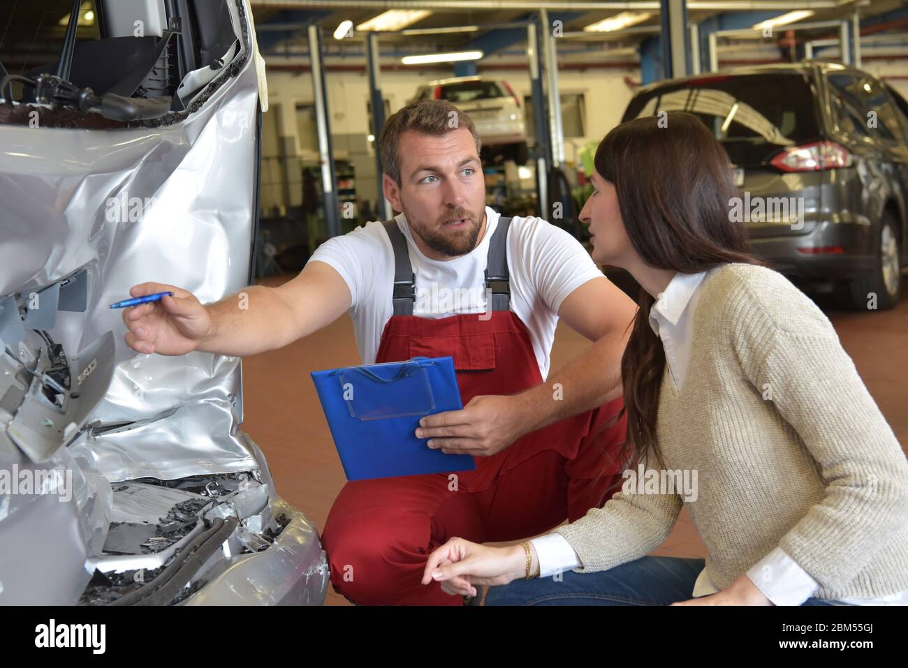 Kundendienst: Kfz-Mechaniker und Frau diskutieren nach einem Verkehrsunfall die Reparatur des Autos Stockfoto