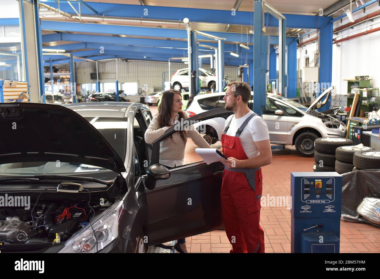 Mechaniker und Kunde sprechen in einer Werkstatt, um ein Fahrzeug zu reparieren Stockfoto