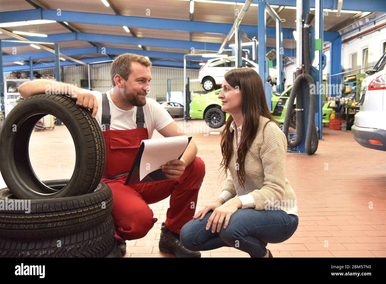 Mechaniker und Kunde sprechen in einer Garage miteinander - Reifen vom Auto wechseln Stockfoto