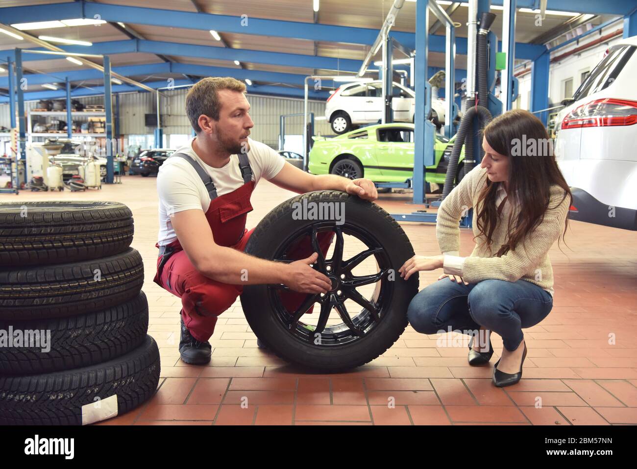 Mechaniker und Kunde sprechen in einer Garage miteinander - Reifen vom Auto wechseln Stockfoto