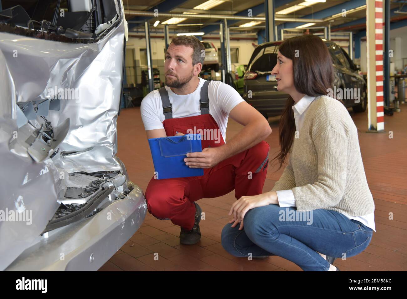 Kundendienst: Kfz-Mechaniker und Frau diskutieren nach einem Verkehrsunfall die Reparatur des Autos Stockfoto