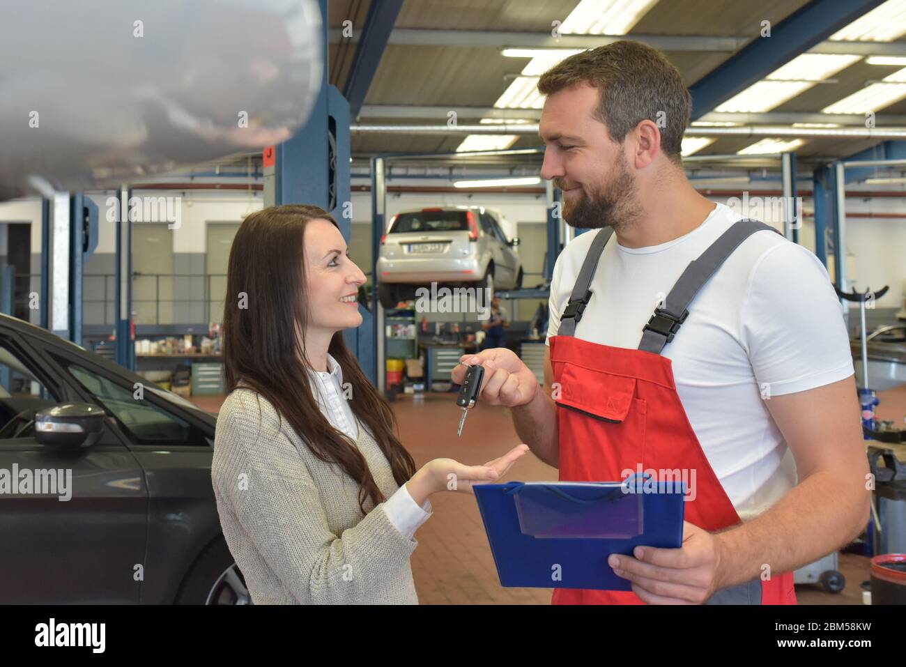 Kundendienst: Kfz-Mechaniker und Kunde besprechen die Reparatur eines Fahrzeugs vor Ort Stockfoto