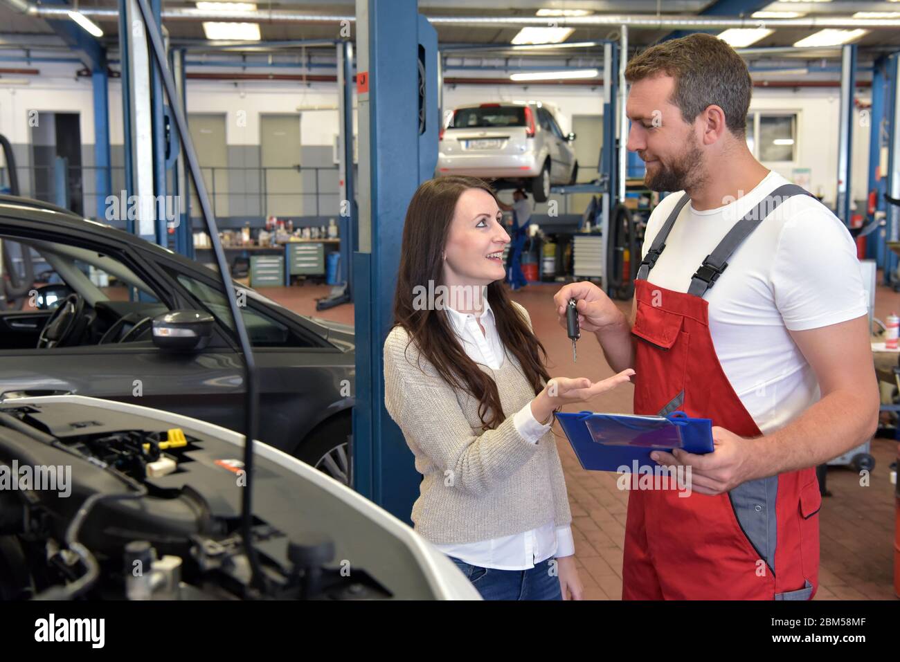 Mechaniker und Kunde sprechen in einer Werkstatt, um ein Fahrzeug zu reparieren Stockfoto