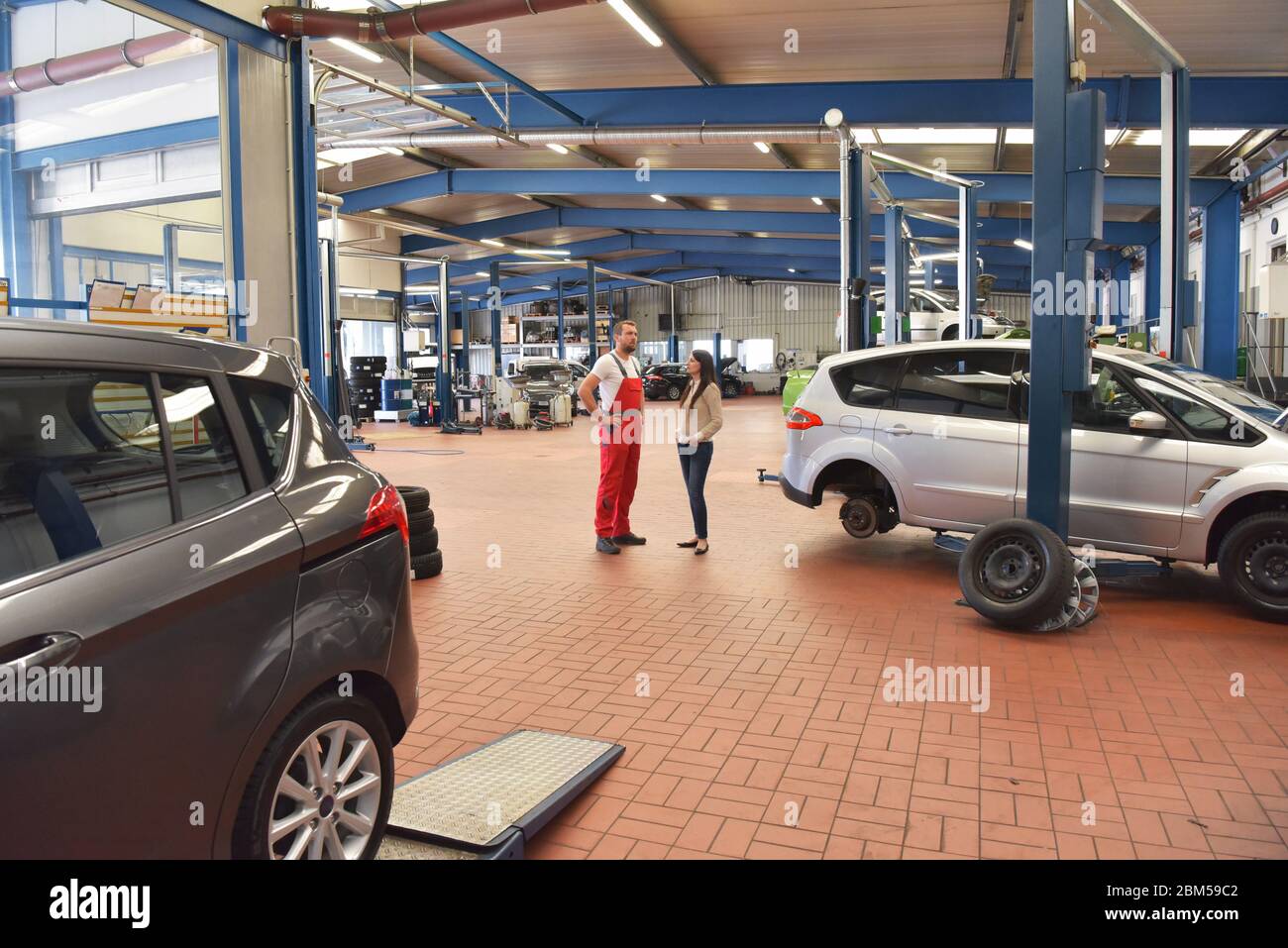 Kundendienst: Kfz-Mechaniker und Kunde besprechen die Reparatur eines Fahrzeugs vor Ort Stockfoto