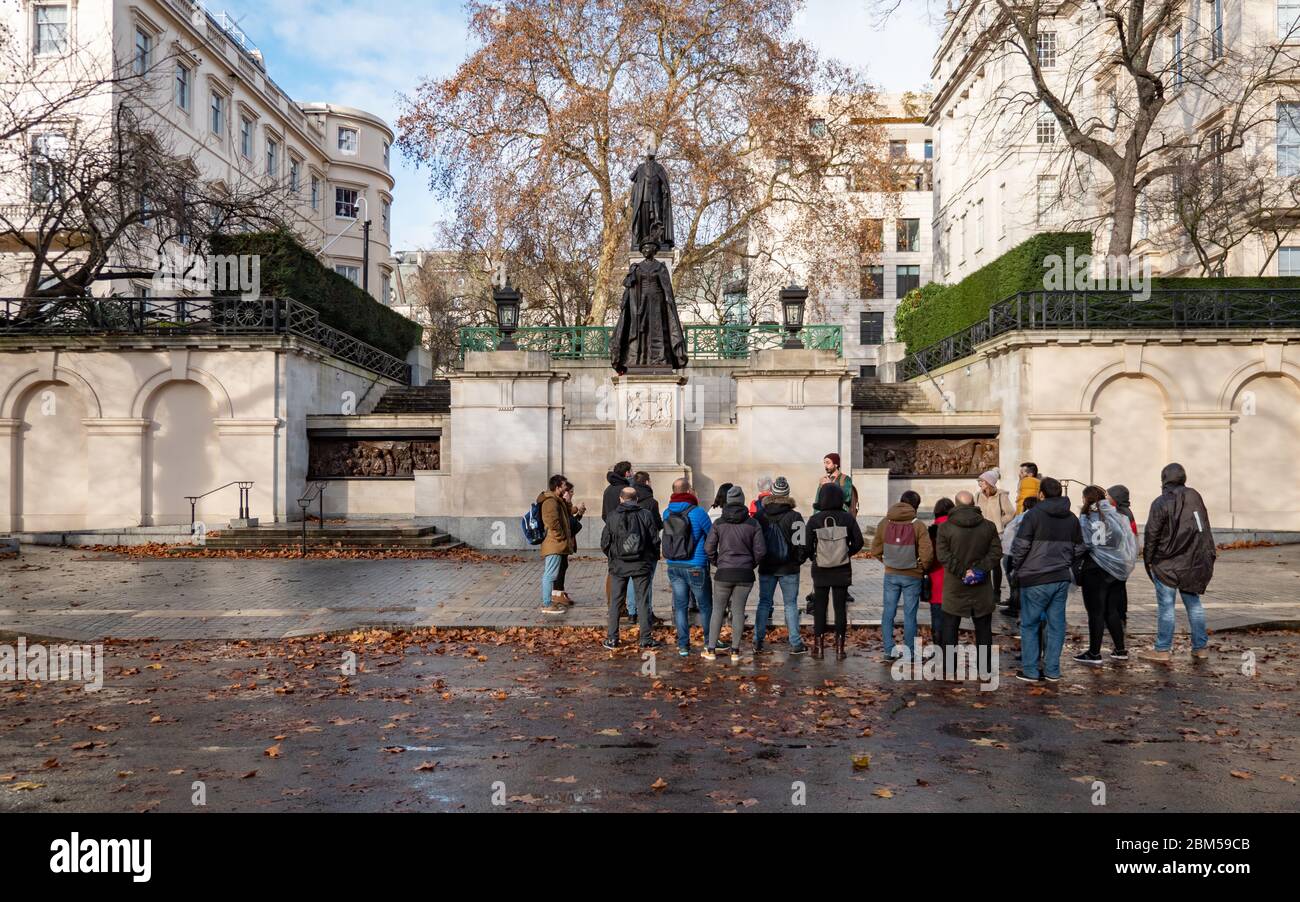 Eine London-Tour-Gruppe auf der Mall, die an einem nassen herbstlichen Londoner Tag die King George VI und Queen Elizabeth Memorials zeigt Stockfoto