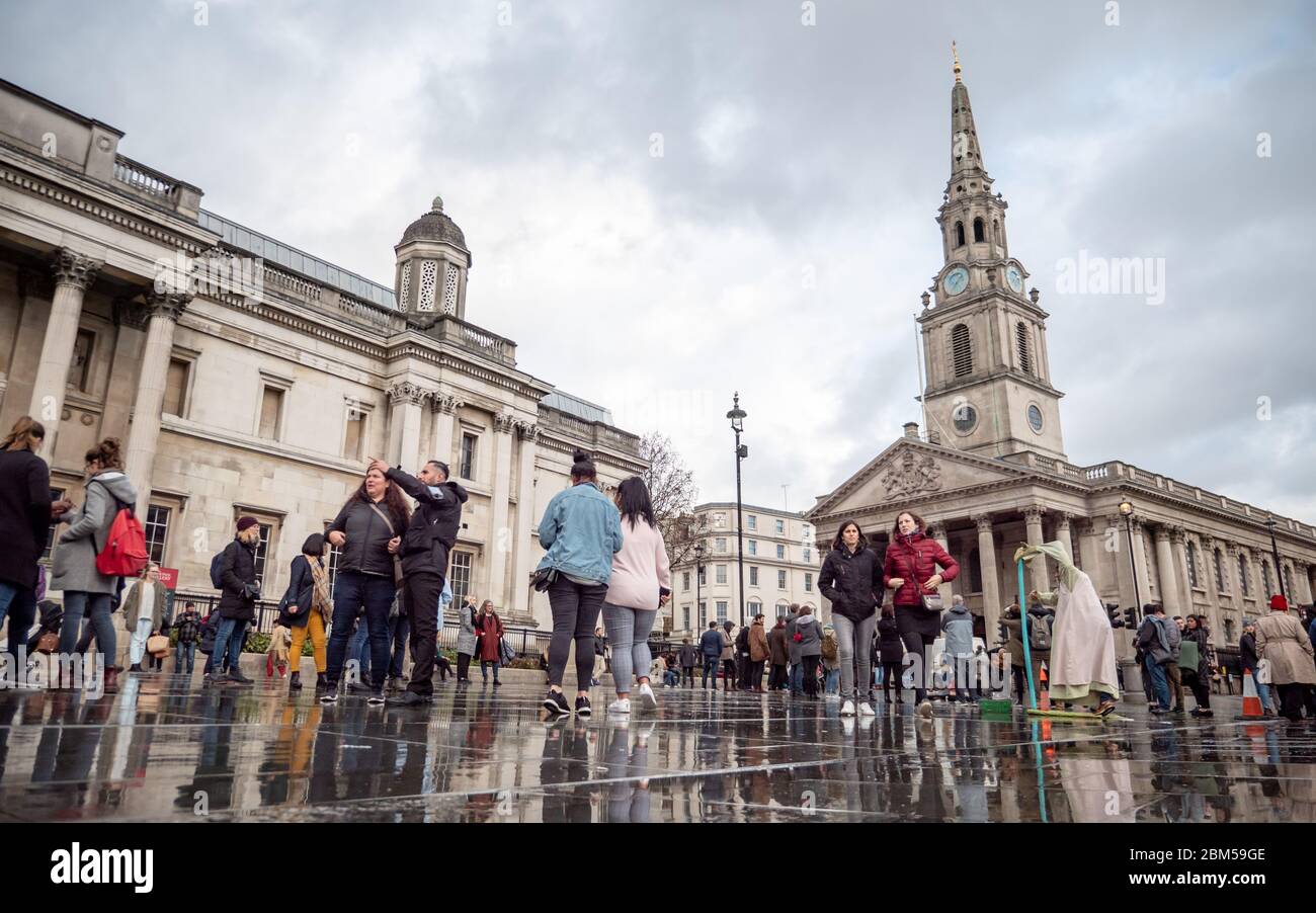 Touristen in einem nassen Trafalgar Square, der von der St. Martin-in-the-Fields Church und der National Gallery, London, dominiert wird. Stockfoto