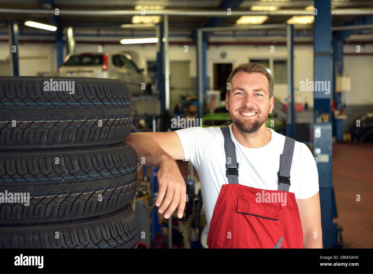 Porträt des erfolgreichen lächelnden Automechanikers in einer Werkstatt auf einem Reifenstapel an seinem Arbeitsplatz Stockfoto