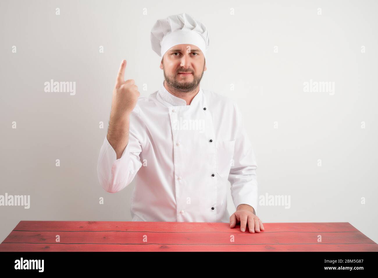 Junger Koch in weißer Uniform, der einen mit dem Finger zählt, der auf einem weißen isolierten Hintergrund posiert Stockfoto