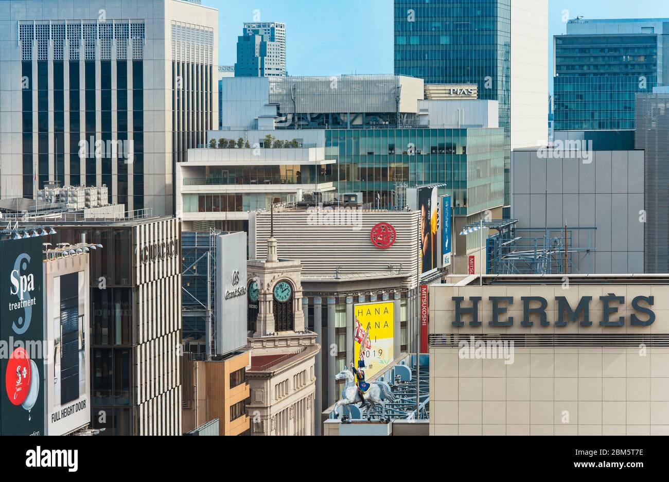 Hochwinkelansicht von Gebäuden und Wolkenkratzern im Tokioter Ginza-Viertel mit der berühmten Wakō-Uhr in der Mitte und Hermes-Reiter im Vordergrund Stockfoto
