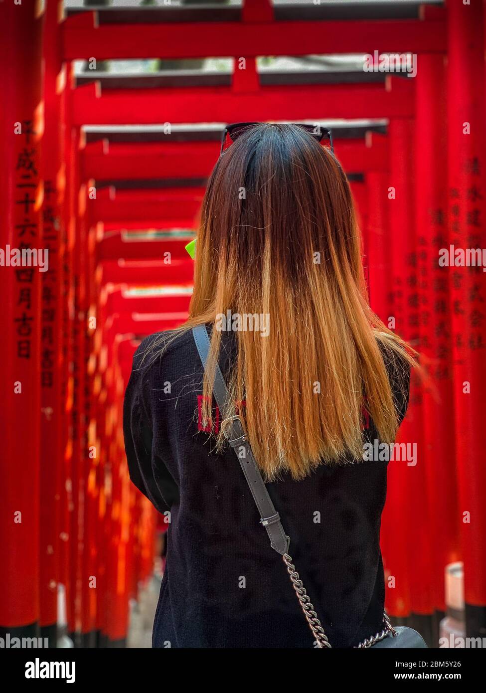 Weibchen mit langen braunen Haaren (zurück zur Kamera), steht am Eingang zu einem Tortunnel am Hie Jinja Schrein, Nagatacho, Tokio. Stockfoto