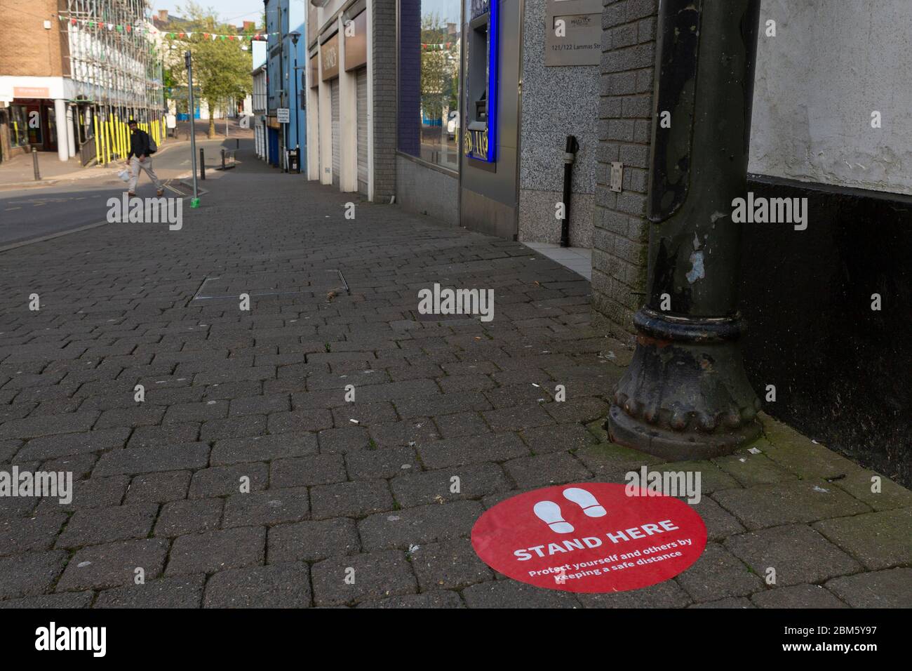 Ein Aufkleber auf dem Bürgersteig vor einer Baugesellschaft / Bank zeigt Kunden, wo sie stehen müssen, um die sozialen Distanzierungsregeln einzuhalten Stockfoto