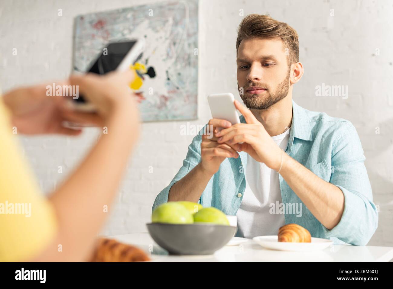 Selektiver Fokus des Mannes mit Smartphone in der Nähe Freundin beim Frühstück in der Küche Stockfoto