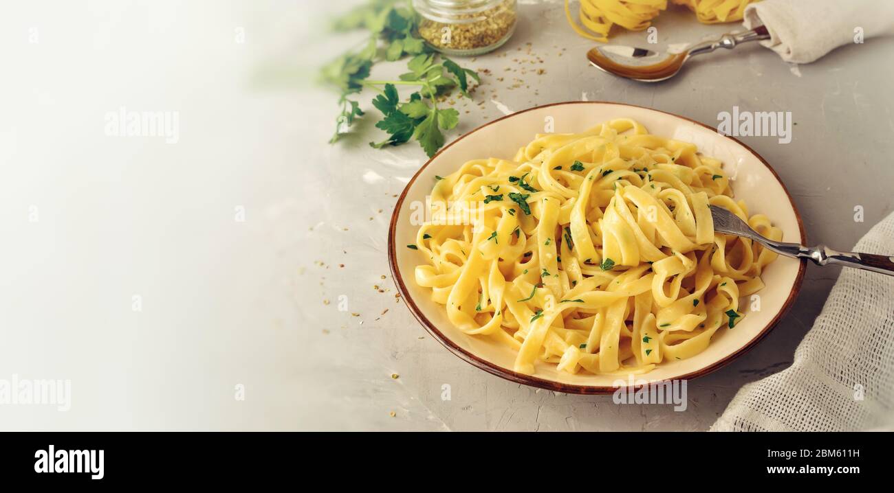 Italienische Pasta in einem Teller mit Gabel. Fettuccini Pasta mit Käse, Sahne, Petersilie, auf einem hellen Hintergrund. Freier Platz für Text. Stockfoto