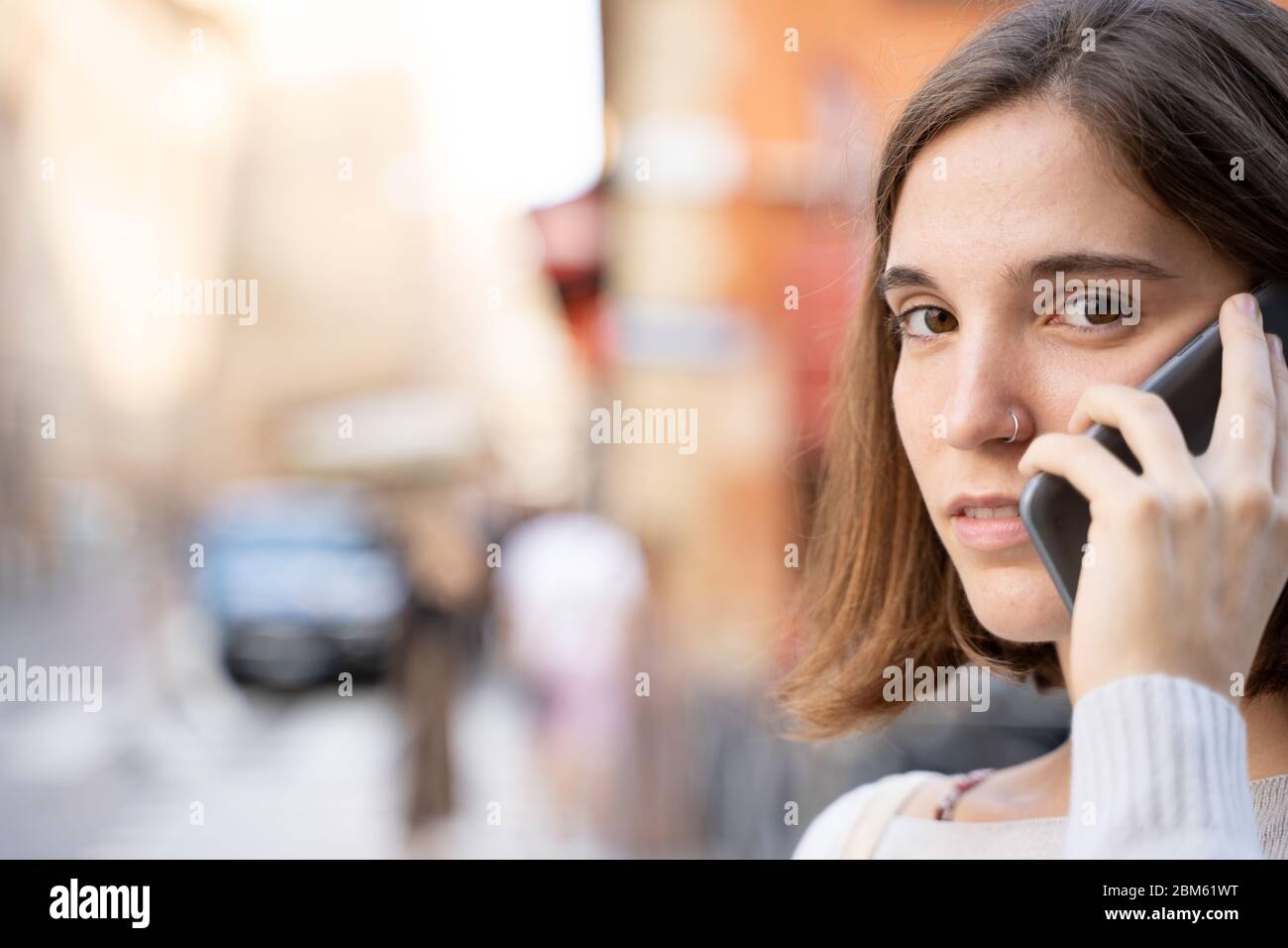 Junge Frau mit einer halben Mähne und einer durchbohrten Nase, die mit einem Smartphone mit besorgtem Ausdruck auf der Straße spricht Stockfoto