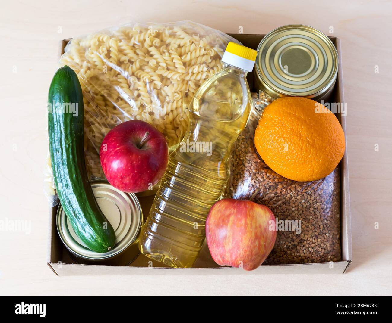 Lebensmittelspende-Box für Menschen mit Pflanzenöl, Gurke, Orangen, Apfel, Makkaroni, Konserven, Buchweizen während der Isolierung des Hauses Stockfoto