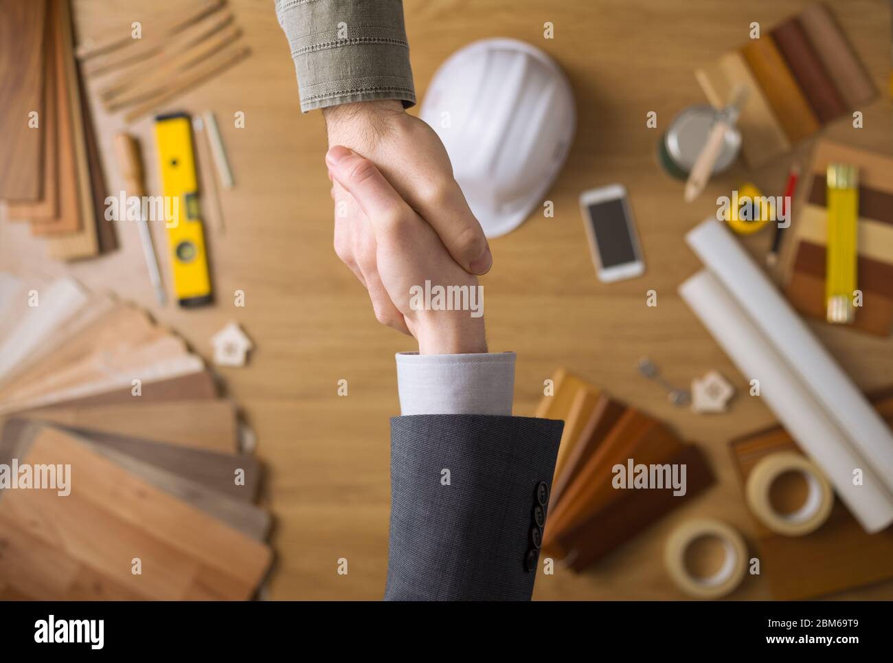 Bauingenieur und Geschäftsmann Händeschütteln Draufsicht hautnah, Desktop mit Arbeitsgeräten und Holz Farbfelder auf Hintergrund Stockfoto