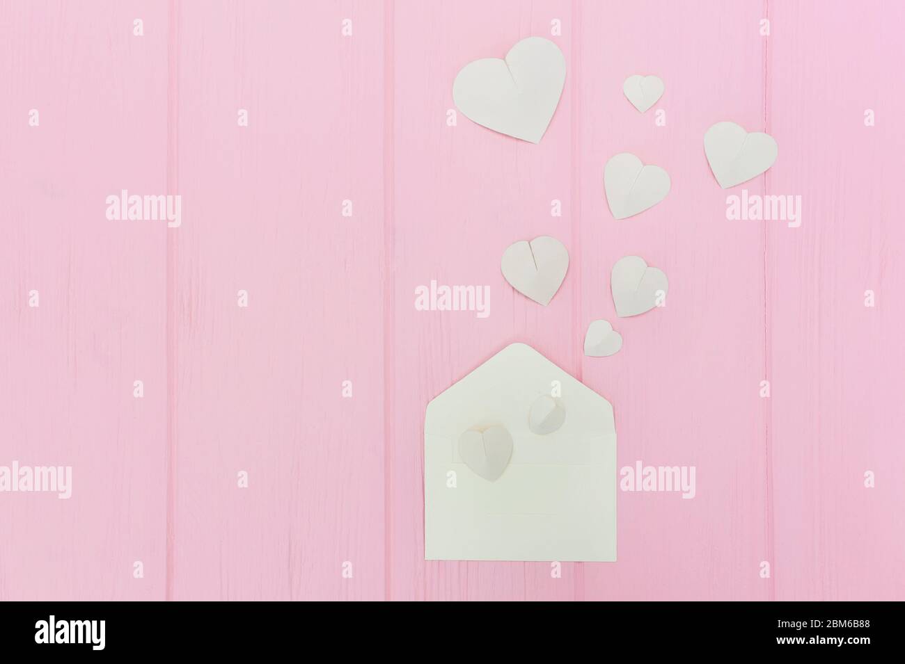 Valentinstag Grußkarte Umschlag mit Herzen. Weiße Herzen ergiessen sich aus dem Umschlag auf rosa Holzhintergrund. Kopierbereich. Herzen fliegen aus Stockfoto