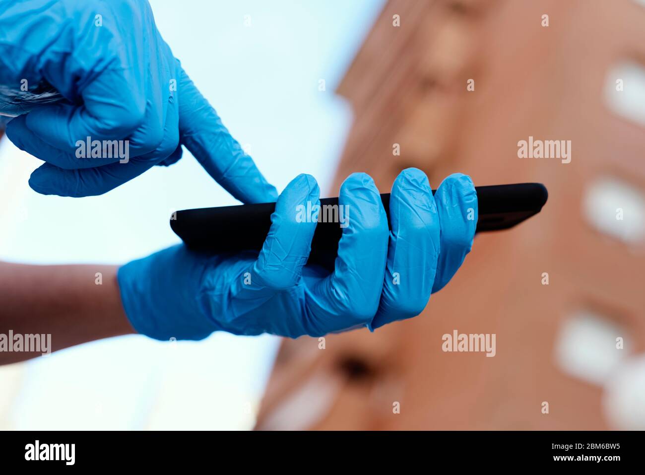 Nahaufnahme eines jungen kaukasischen Mannes auf der Straße, der blaue Latexhandschuhe trägt und sein Smartphone benutzt Stockfoto