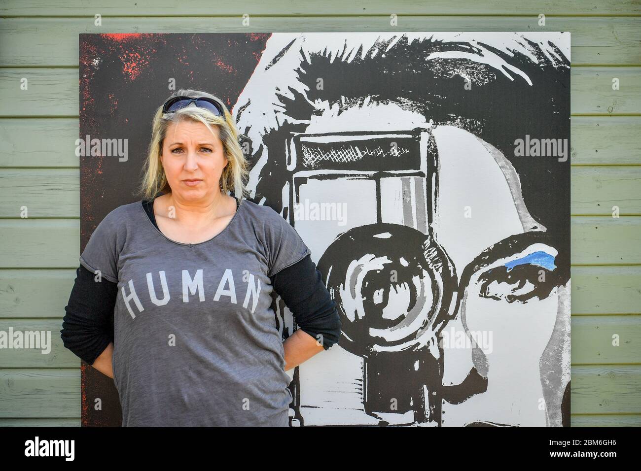 Die Künstlerin Shelley Dyer Gibbins, 47, aus dem Dorf Croscombe, in der Nähe von Wells, sitzt neben einem ihrer Werke mit dem Titel Cinegirl, Sie hat für alle 600 Einwohner des Dorfes Somerset Designer-Gesichtsmasken entworfen, sowohl aus medizinischem Maskenmaterial als auch aus einigen ihrer Kunstdruckmaterialien, die sie hinterlassen hatte. Stockfoto