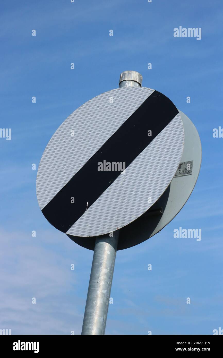 Ende der Beschränkung - Straßenverkehrsschild zeigt das Ende einer Geschwindigkeitsbegrenzung und dass nationale Geschwindigkeitsbegrenzung gilt mit einem blauen Himmel im Hintergrund. Stockfoto