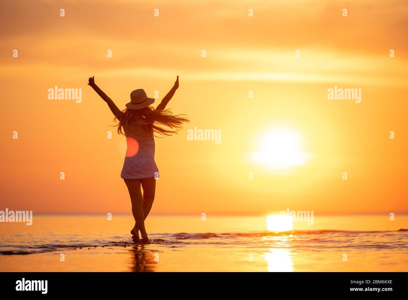 Junge glückliche Mädchen steht oder tanzt am Sonnenuntergang Strand mit erhobenen Armen Stockfoto