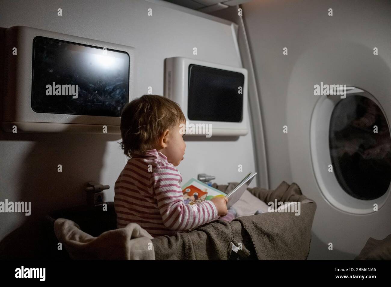 Konzept des bequemen Flugs mit Kleinkind. Kleines süßes Kleinkind, das in einer Liegewanne sitzt und ein Buch liest. Stockfoto