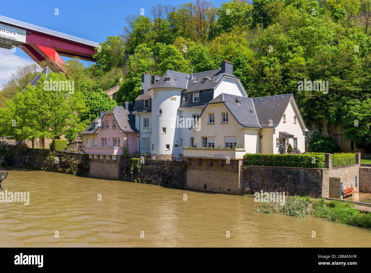 Fluss Alzette in Pfaffenthal, Luxemburg, mit Häusern am Flussufer. Im Hintergrund Vauban Tower und Grand Herzogin Charlotte rote Brücke. Stockfoto