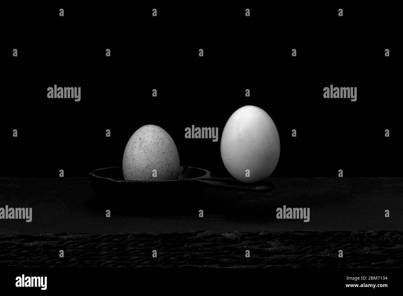 Zwei Eier auf einer Gusseisenpfanne balanciert, eines an der Spitze des Griffs und das andere in der Pfanne, das eine an der Spitze wird nicht verursachen, die andere in t Stockfoto