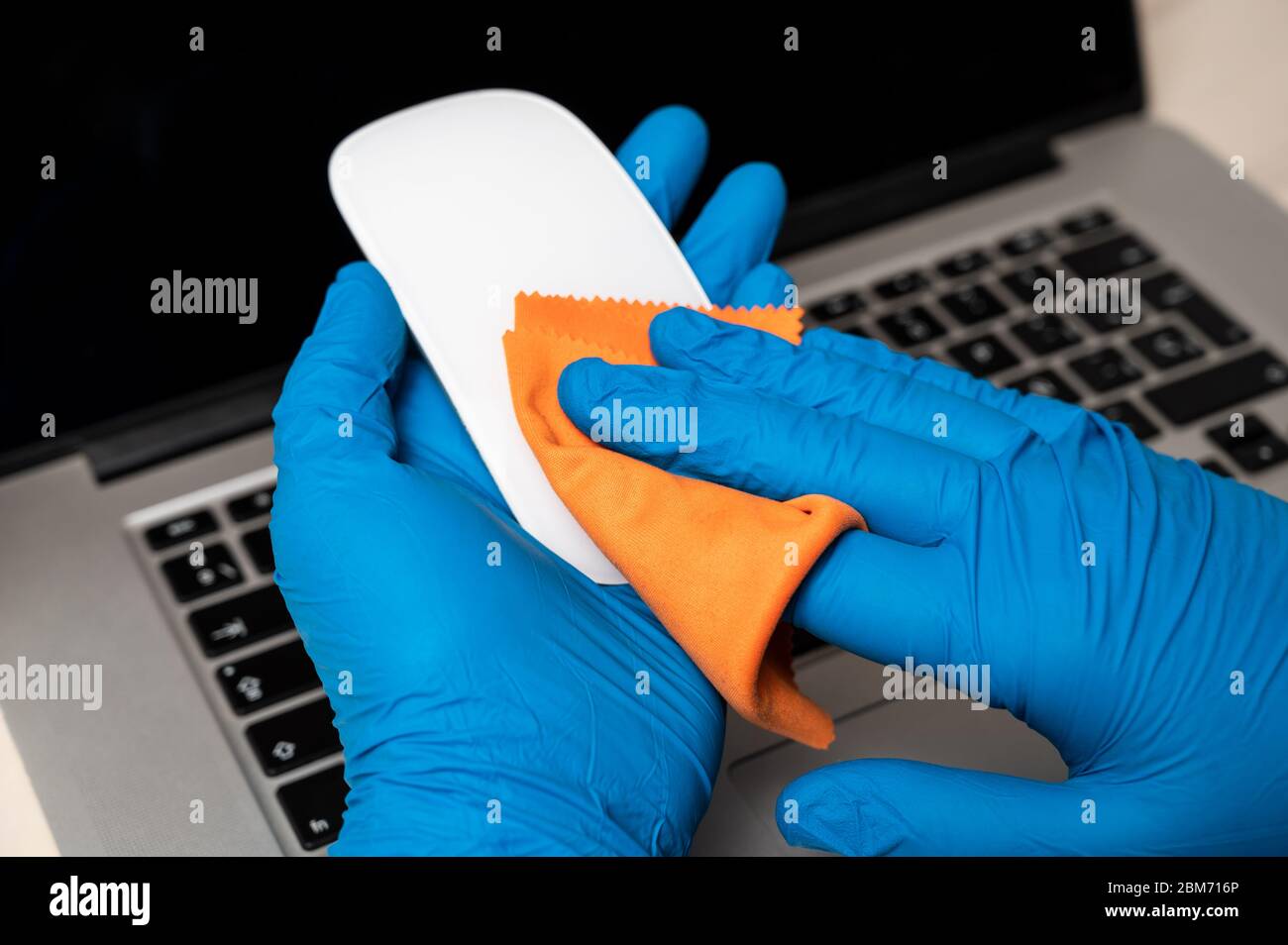 Reinigen und Desinfizieren einer Maus mit Schutzhandschuhen. Reinigen der Oberflächen von Notebook-Computern von Viren, Mikroben und Schmutz im Büro für sicheres Arbeiten. C Stockfoto