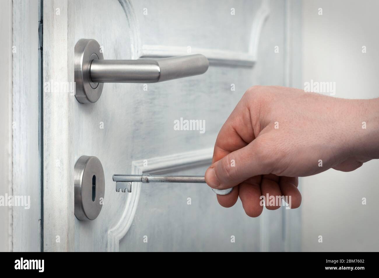Kaukasischer Mann öffnet eine moderne Tür mit Metallgriff mit einem alten rostigen Schlüssel Stockfoto
