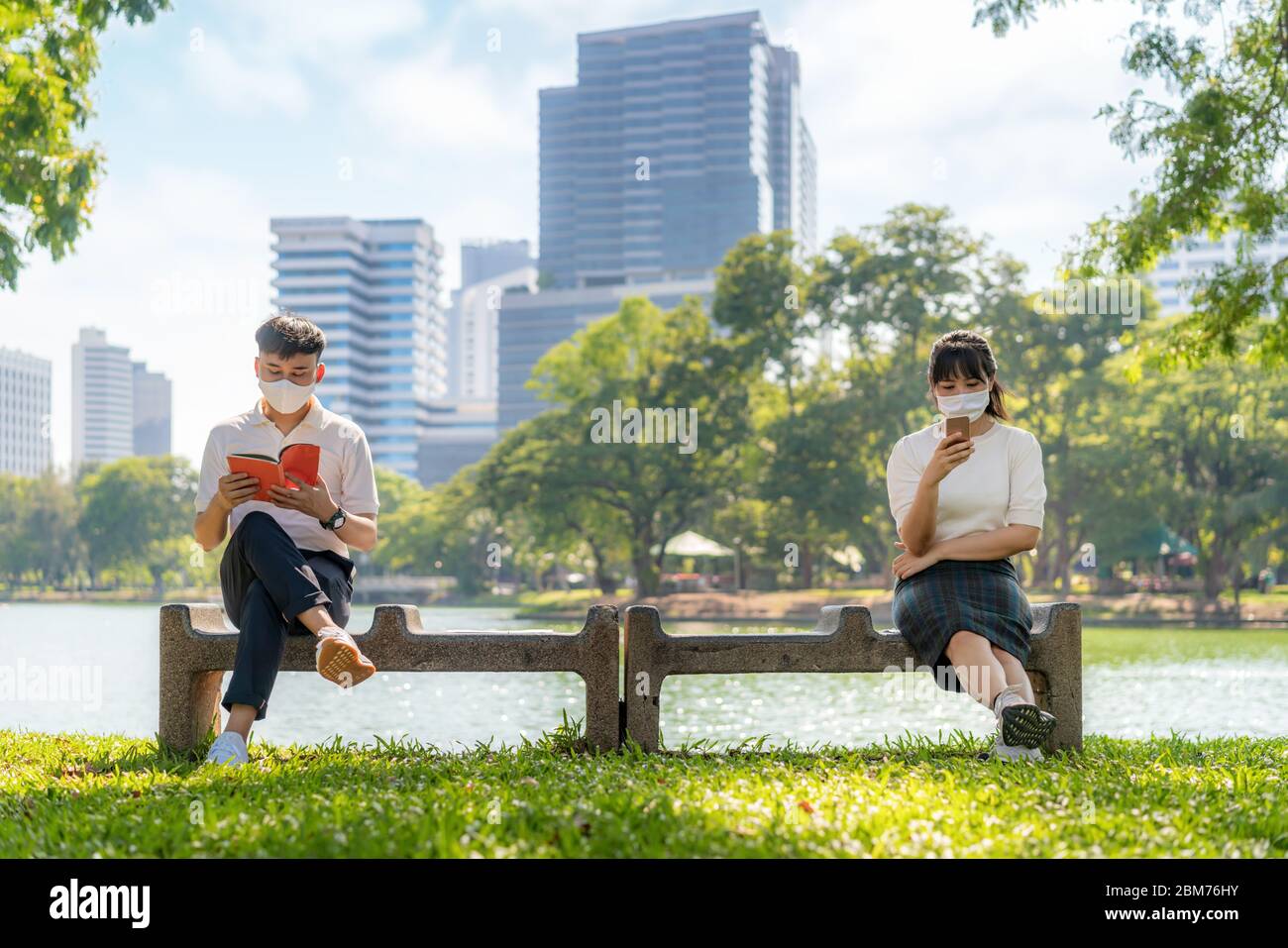 Asiatische junge Mann und Frau Buch lesen und chatten in Smartphone und Maske tragen sitzende Abstand von 6 Fuß Abstand vor COVID-19 Viren f schützen Stockfoto
