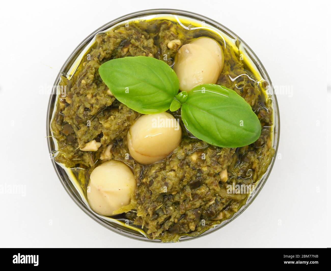 Eine Schale aus grüner Pesto-Sauce, gekrönt mit Macadamia-Nüssen und Basilikumblättern, auf WEISSEM Hintergrund, London, Großbritannien Stockfoto