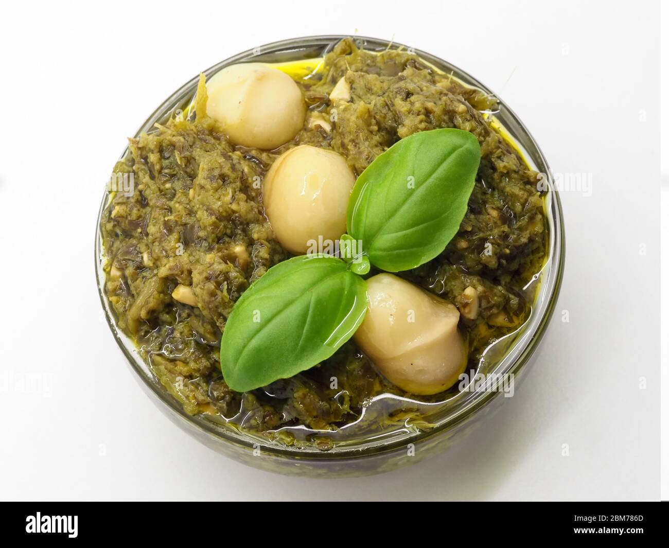 Eine Schale aus grüner Pesto-Sauce, gekrönt mit Macadamia-Nüssen und Basilikumblättern, auf WEISSEM Hintergrund, London, Großbritannien Stockfoto